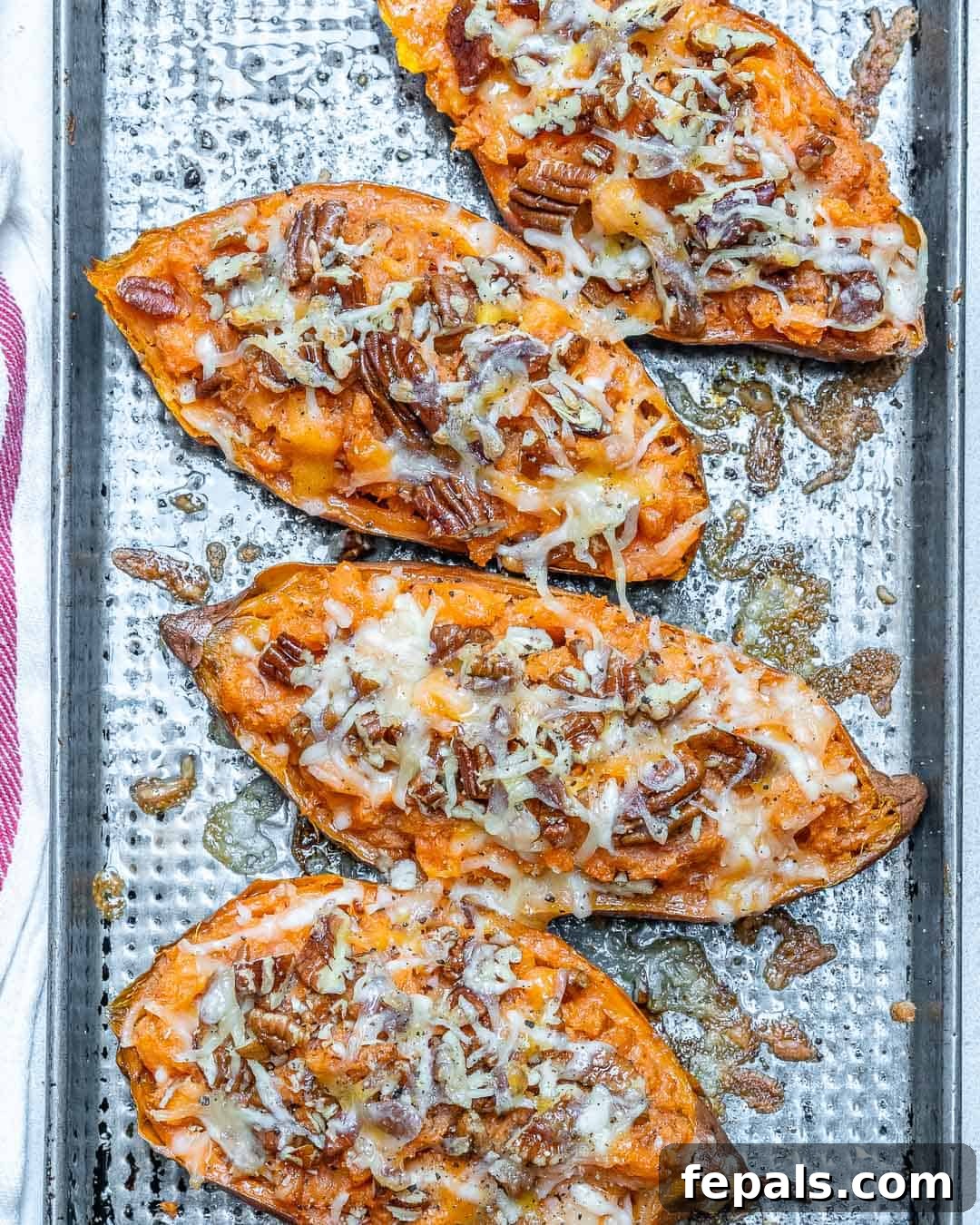 Ultimate Twice-Baked Sweet Potatoes 2 Four golden-brown twice-baked sweet potatoes arranged on a baking sheet, glistening with melted cheese and adorned with chopped pecans. The inviting aroma is almost palpable.
