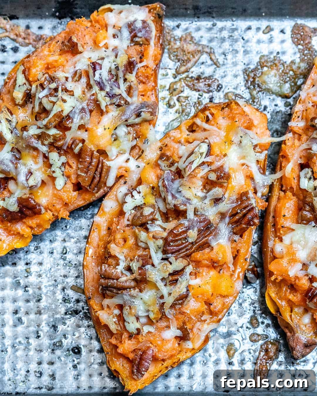 Ultimate Twice-Baked Sweet Potatoes 3 Three perfectly baked sweet potatoes, halved and stuffed, adorned with a sprinkle of chopped pecans and a tempting layer of melted cheese, waiting to be enjoyed.