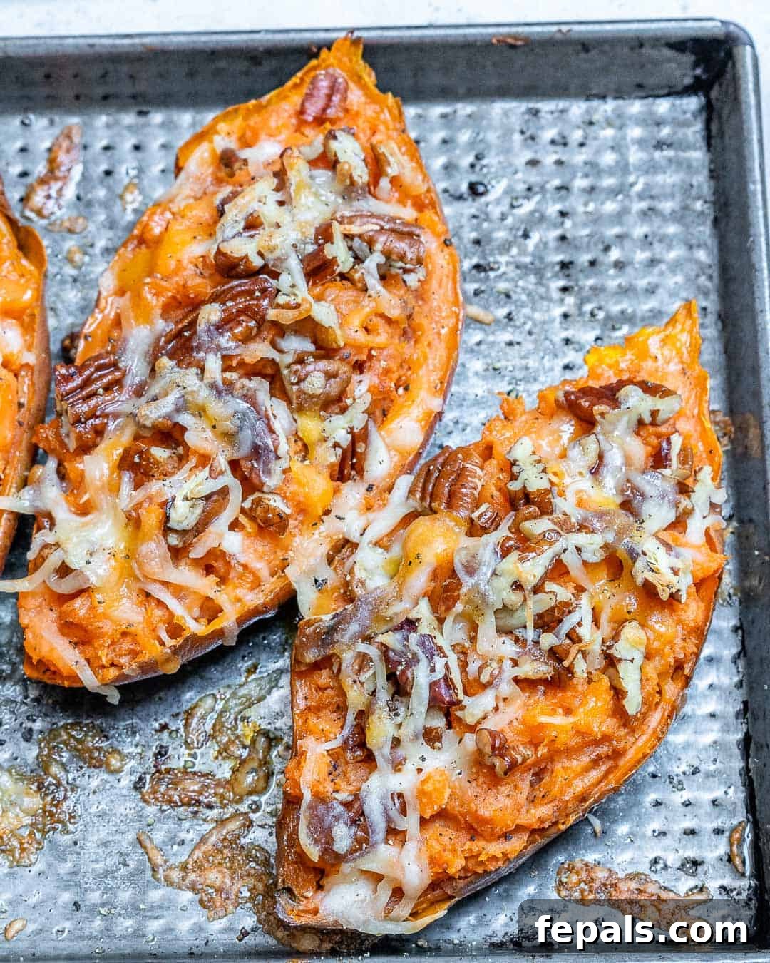 Ultimate Twice-Baked Sweet Potatoes 6 Two vibrant twice-baked sweet potatoes, generously topped with a sprinkle of chopped pecans and a rich layer of melted cheese, displayed on a baking sheet, ready to be served and savored.