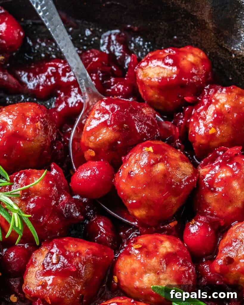 spoon grabbing 2 drenched chicken meatball with cranberry sauce