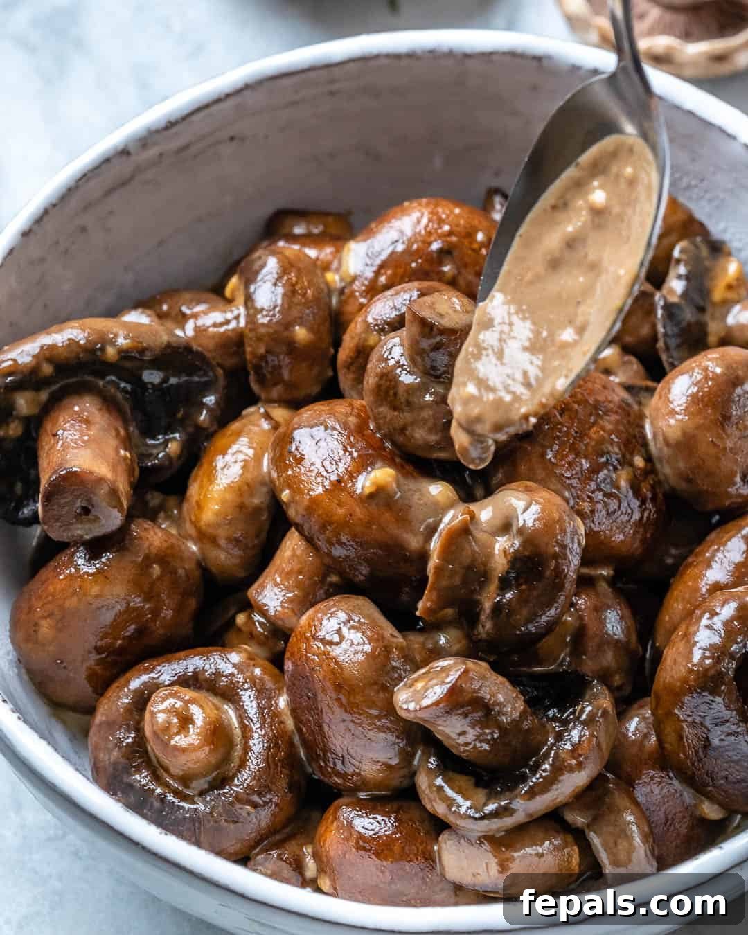 spoon pouring creamy sauce over sauteed mushrooms in a bowl.