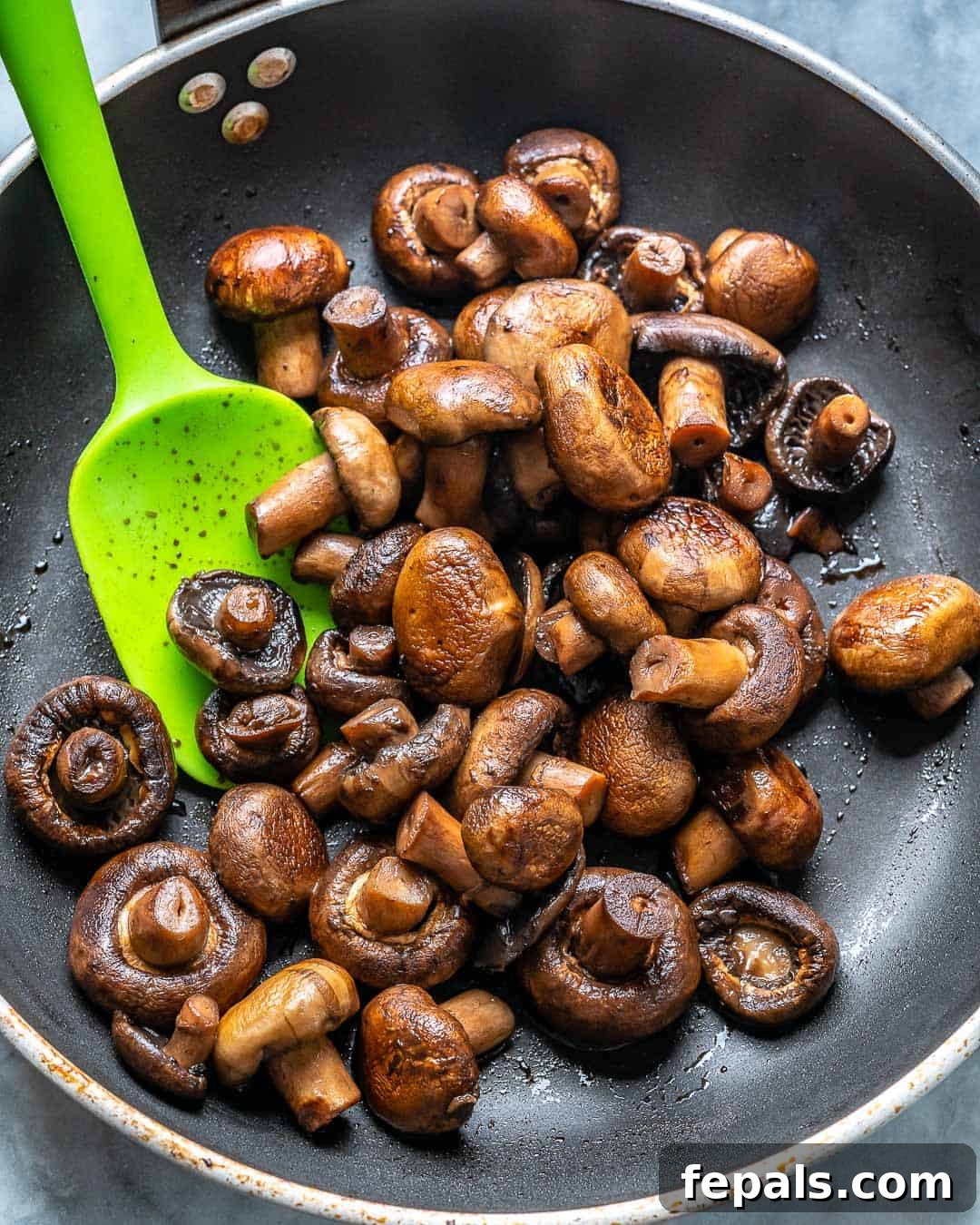 sauteed mushrooms in a black frying pan with a green spatula in pan.