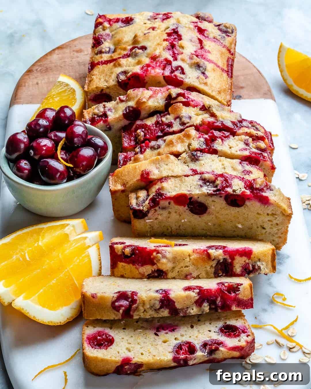 Zesty Cranberry Orange Loaf 2 Slices of moist Cranberry Orange Bread with fresh cranberries and orange zest on a wooden board
