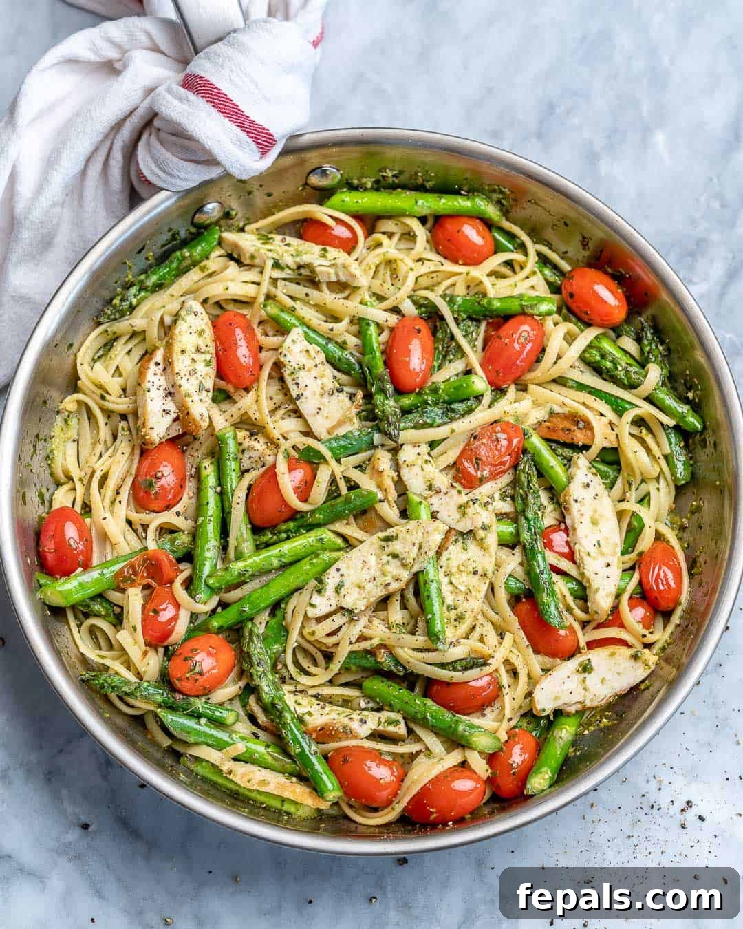 Spring Chicken Asparagus Pasta 2 Top view of a stainless steel skillet brimming with Asparagus Pesto Chicken Pasta, garnished with bright cherry tomatoes and fresh basil.