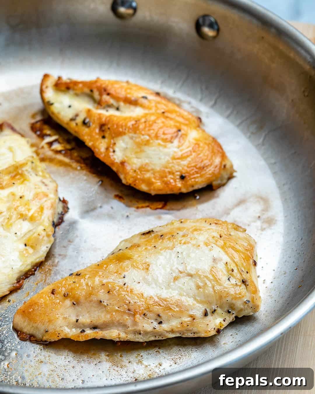 Three perfectly seared chicken breasts resting in a pan, ready to be sliced.
