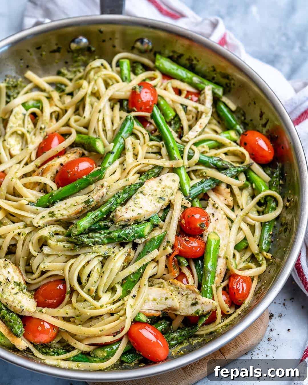 Spring Chicken Asparagus Pasta 5 Top view of a stainless steel skillet filled with vibrant green pesto linguine, tender chicken pieces, asparagus, and cherry tomatoes, ready to be served.
