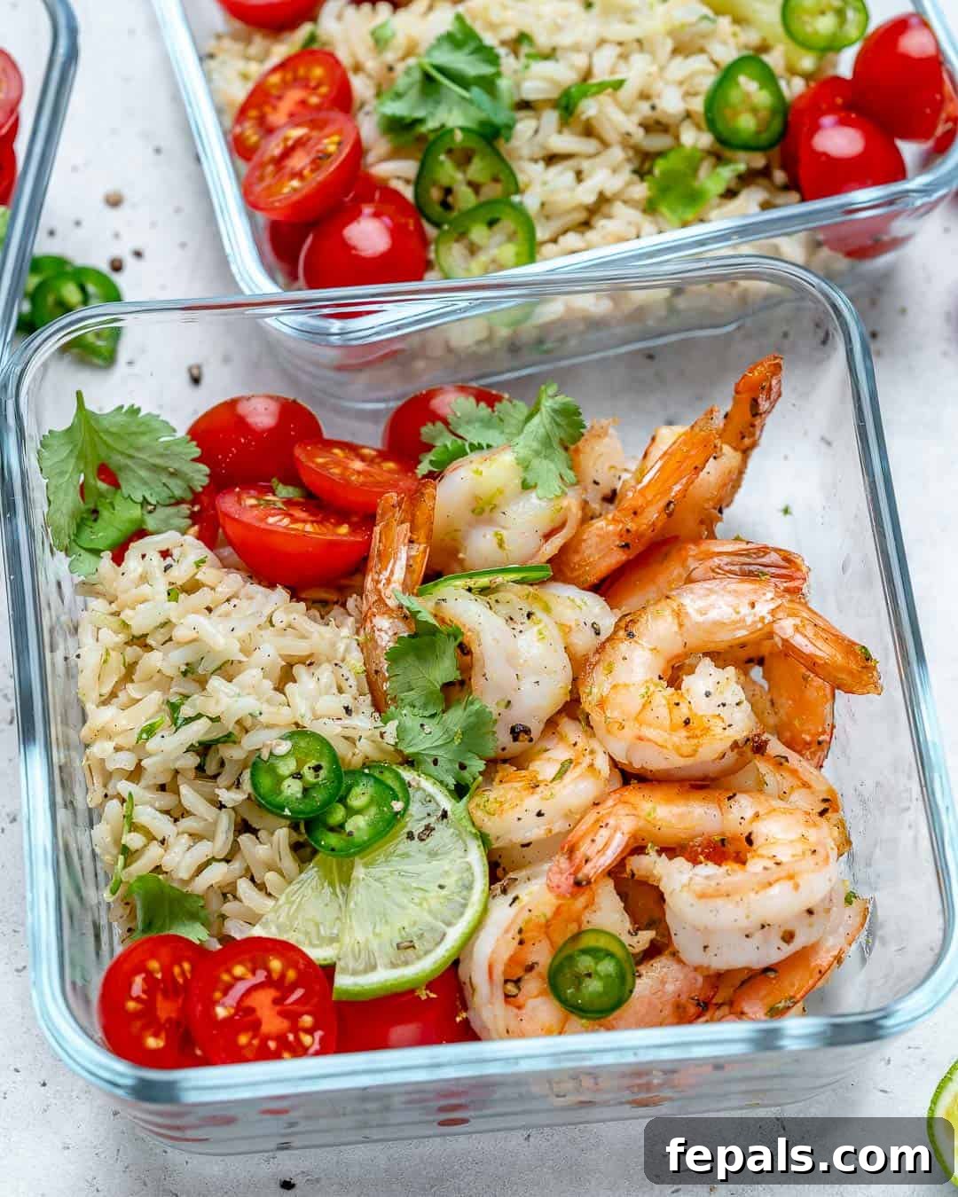 Savory Garlic Shrimp Meal Prep 5 A vibrant and healthy meal prep bowl filled with golden garlic lime shrimp, fluffy brown rice, and fresh cherry tomatoes, garnished with a lime wedge.