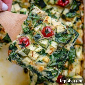 A portion of baked eggs and veggies on a spatula, ready to be served from the quiche.