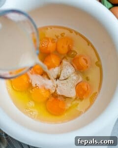 Milk being added to a bowl with raw eggs.