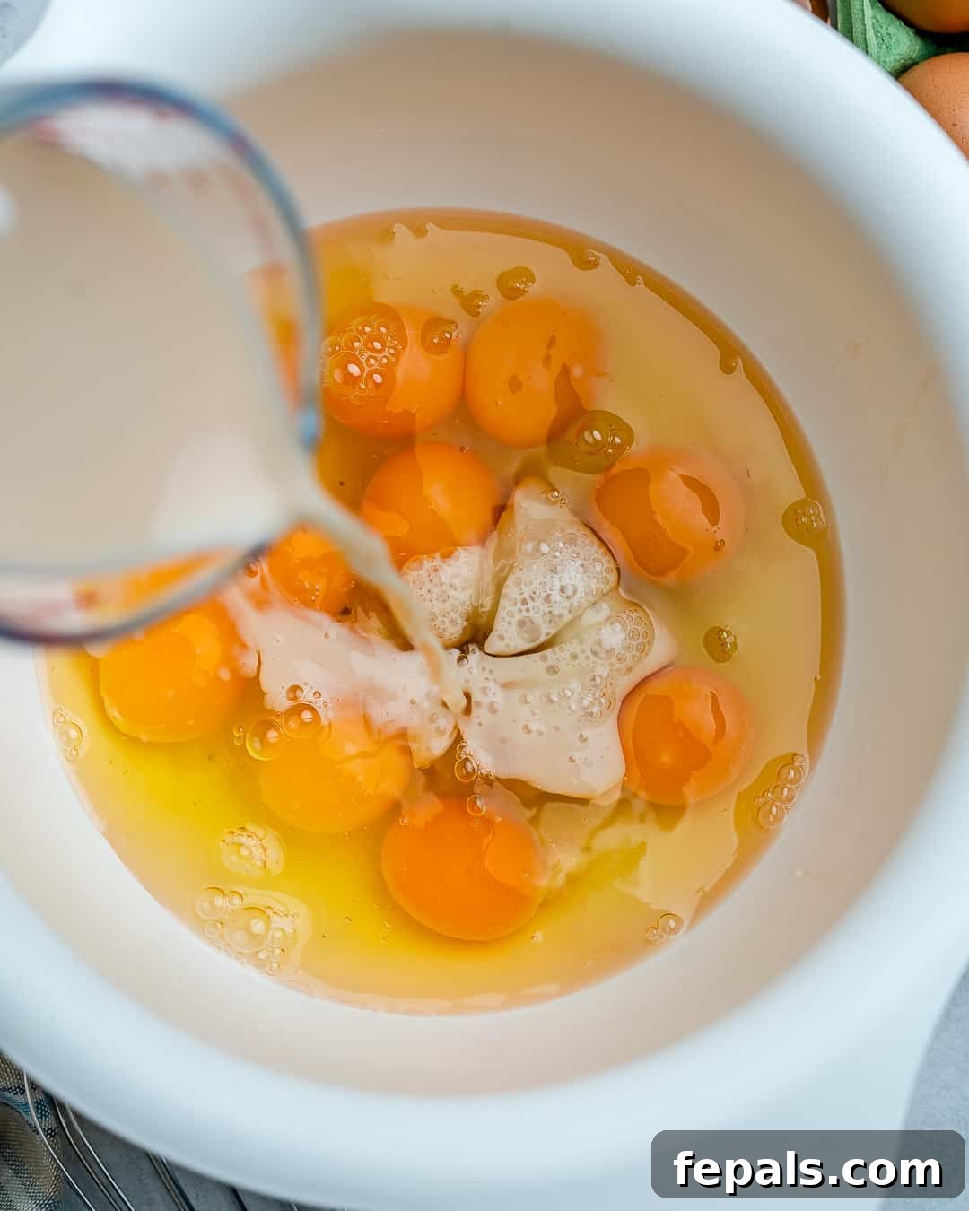 Milk being poured into a bowl with raw eggs, ready to be whisked for the quiche.