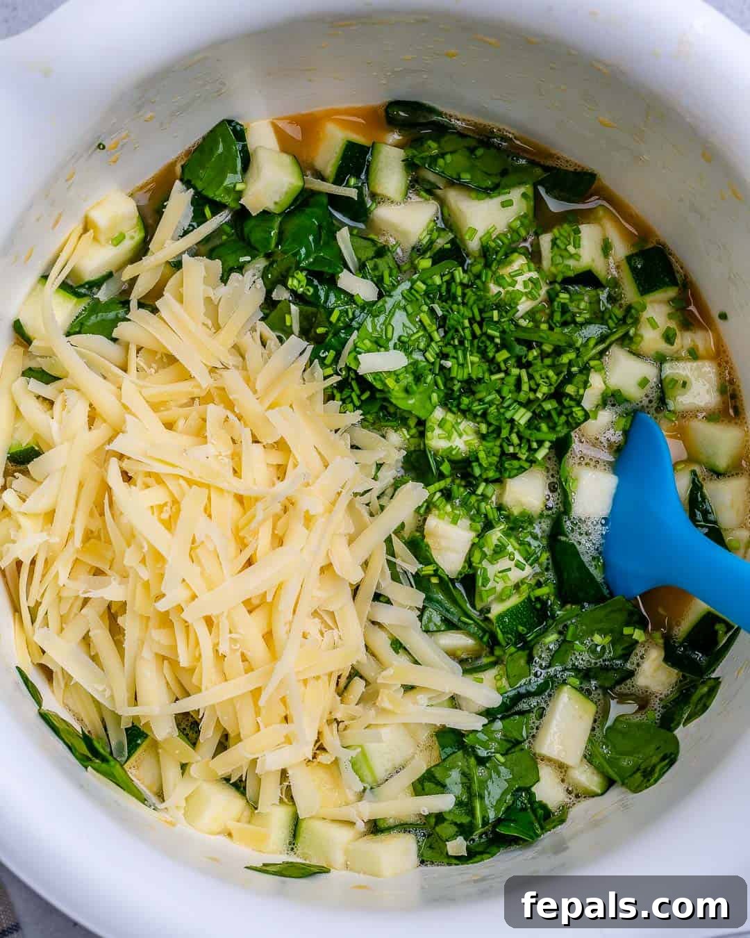 Veggies and shredded cheese added into a bowl with whisked eggs, ready for gentle folding.