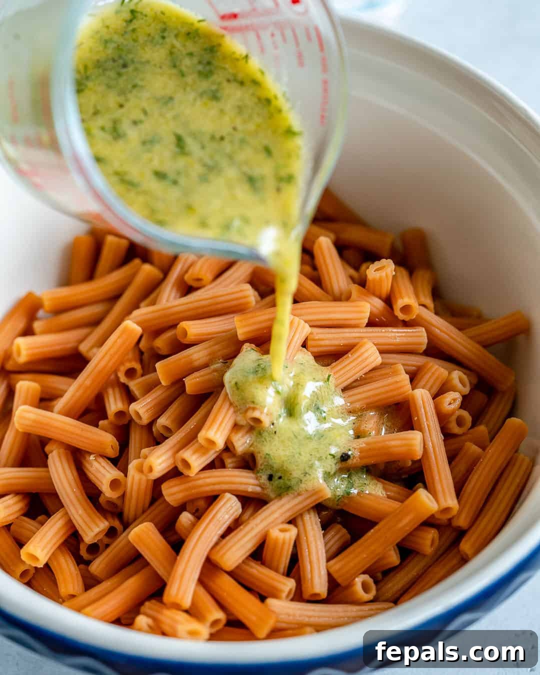 Salmon pasta salad with zesty lemon dill dressing being poured over, creating a tempting visual
