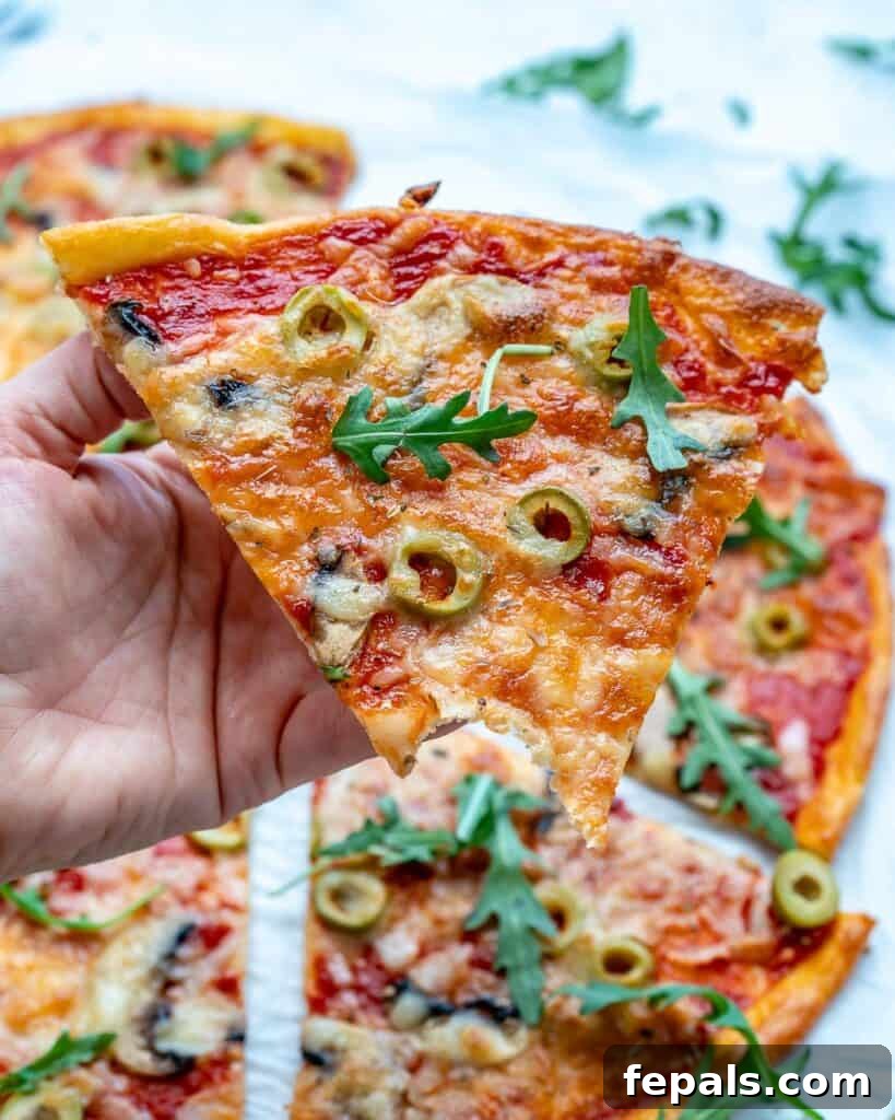 A hand holds a single slice of low-carb pizza, with a bite taken, revealing its thin crust and savory toppings.