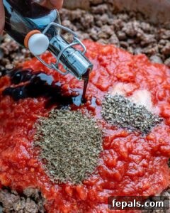 Adding vinegar and tomato sauce to seared meat in a pan.