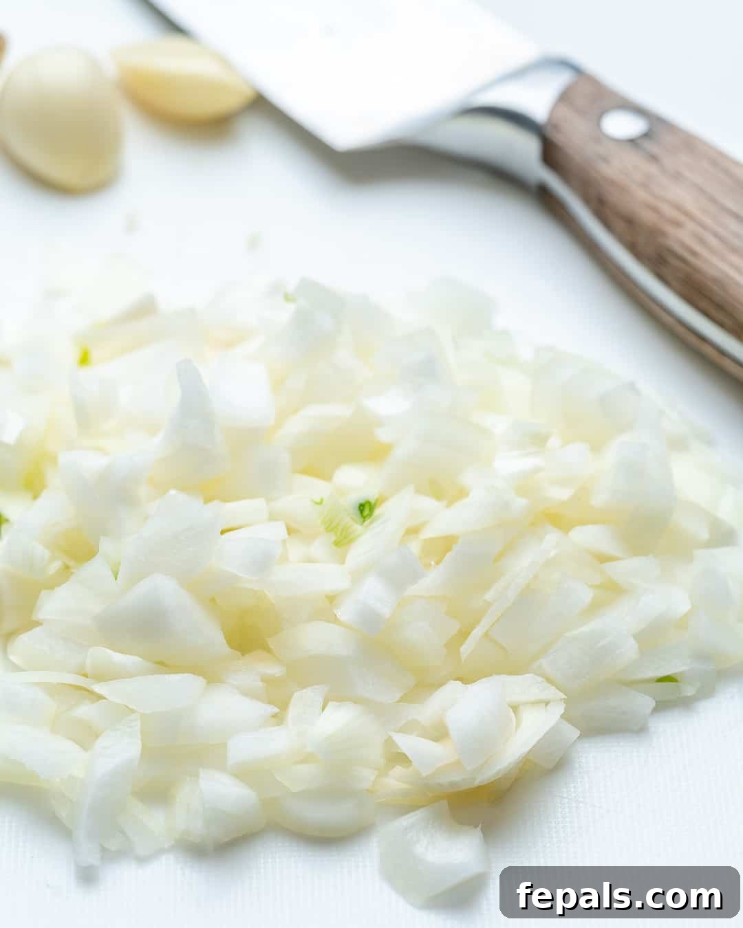 Freshly chopped onions on a wooden cutting board, ready for cooking.