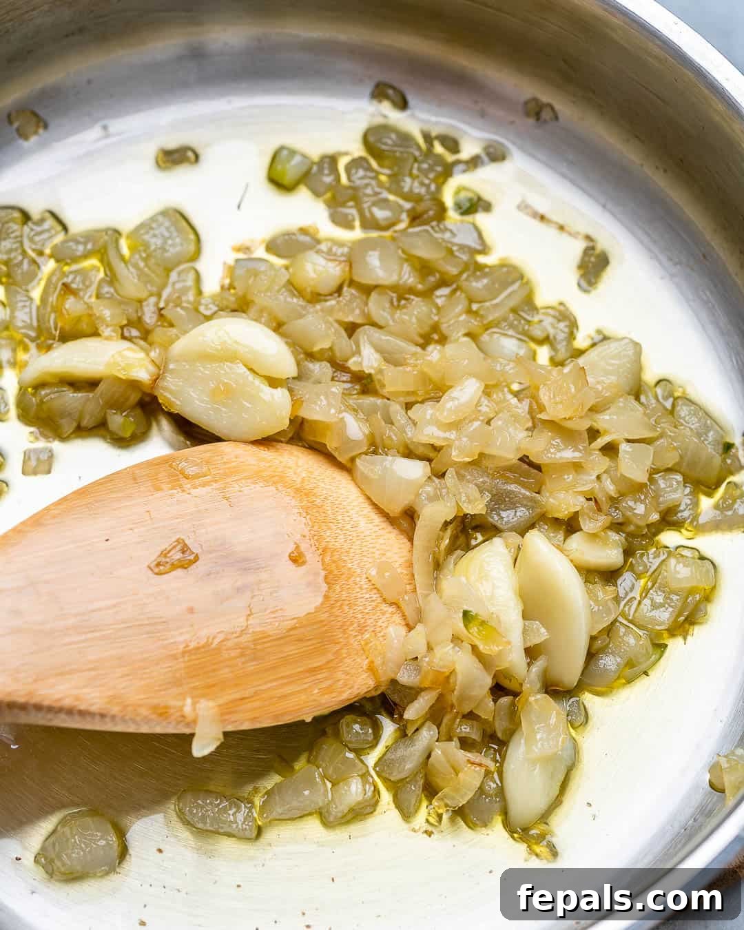 Sautéed diced onions and minced garlic gently cooking in olive oil in a pan.