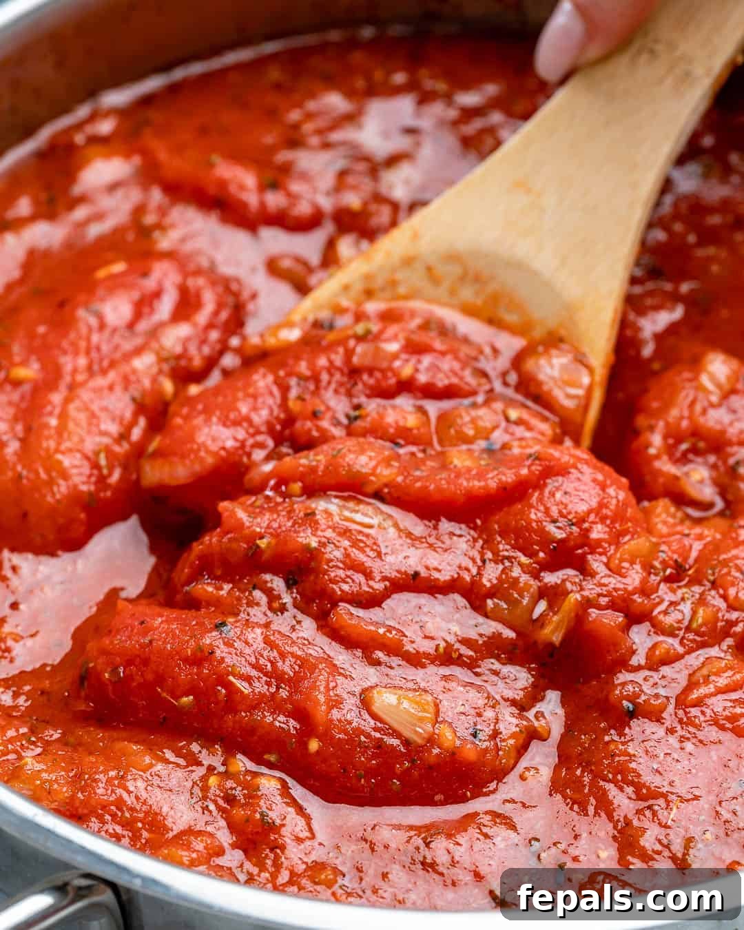 Marinara sauce simmering gently on the stove, with vibrant red tomatoes and green herbs visible.