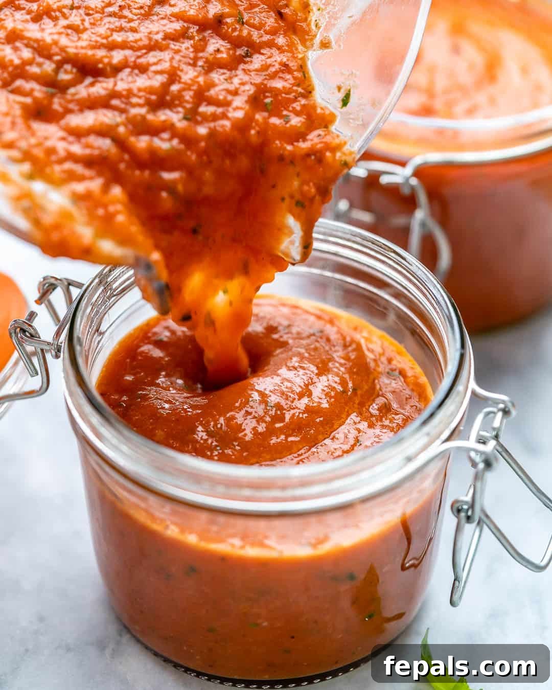 Rich homemade marinara sauce being poured into a clear glass jar.