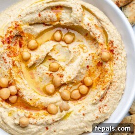 homemade hummus in a white dish with a drizzle of olive oil, chickpeas, and paprika.