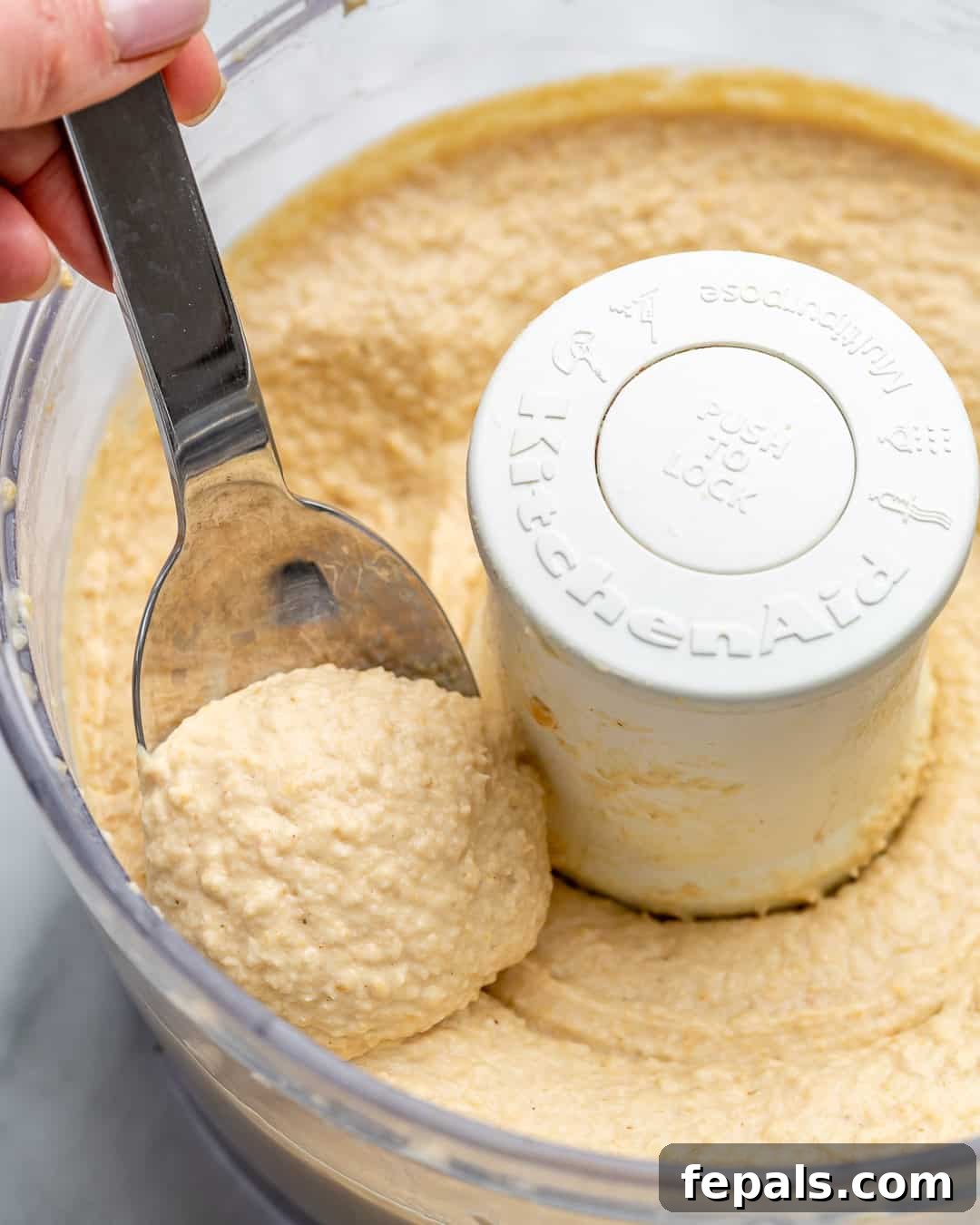 Simple Steps to Creamy Homemade Hummus 7 A spoon scooping perfectly blended, creamy hummus from a food processor.