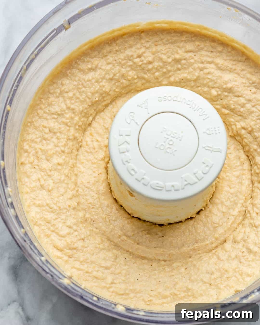 Simple Steps to Creamy Homemade Hummus 8 A close-up of creamy, blended hummus in a food processor, showcasing its smooth texture.