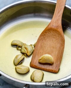 Healthy and Delicious Cauliflower Alfredo Sauce 14 garlic in pan with oil for frying. with wooden spoon in pan