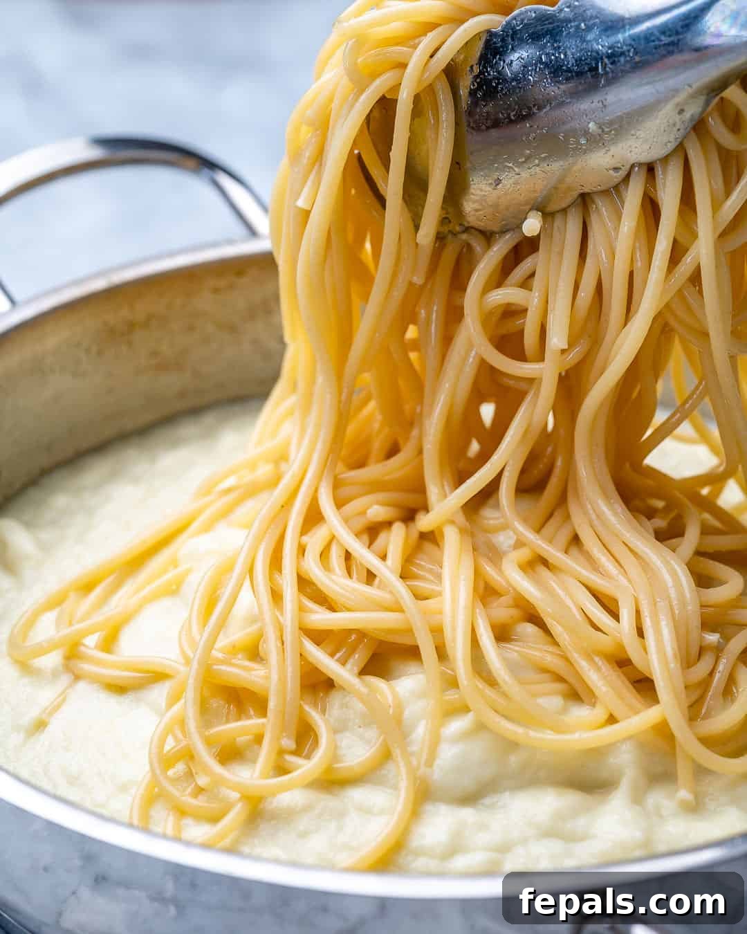 Healthy and Delicious Cauliflower Alfredo Sauce 8 Spaghetti being stirred into creamy Alfredo sauce in a pan