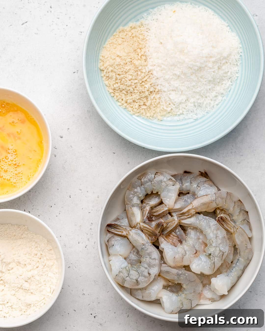 ingredients to make coconut shrimp, a bowl of raw shrimp, shredded coconut, and crumbs 