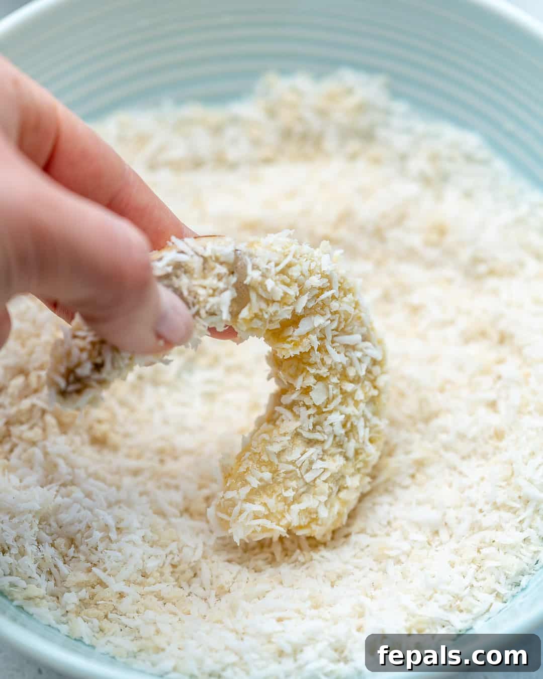 raw shrimp being dipped in coconut breading mic in a bowl