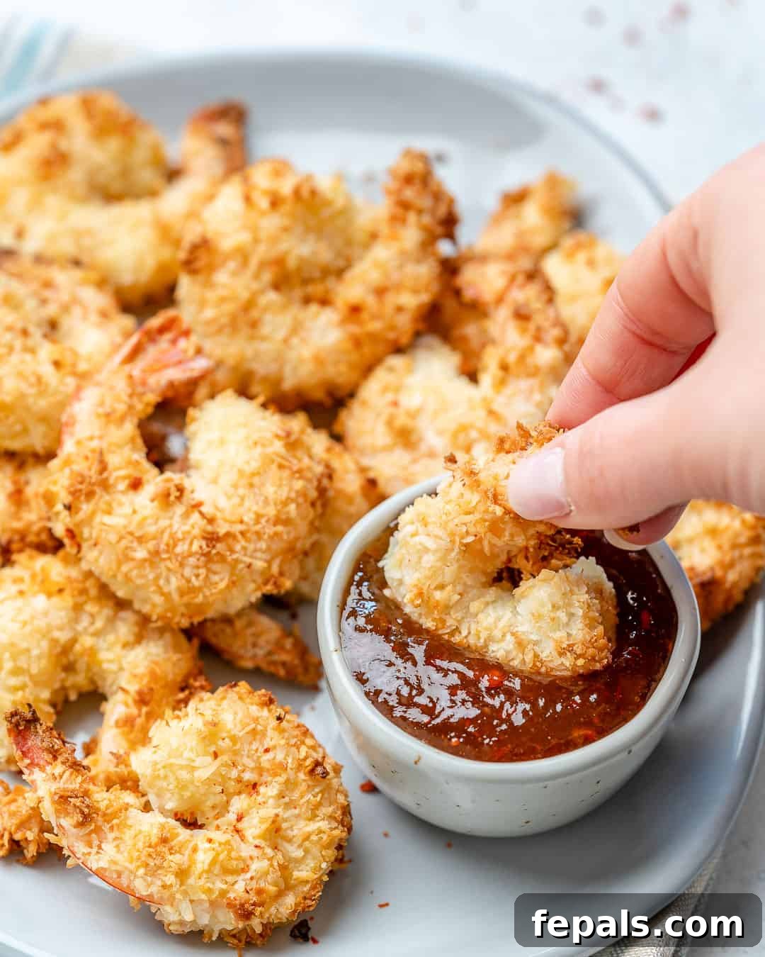 hand holding a coconut shrimp in a dipping sauce bowl.