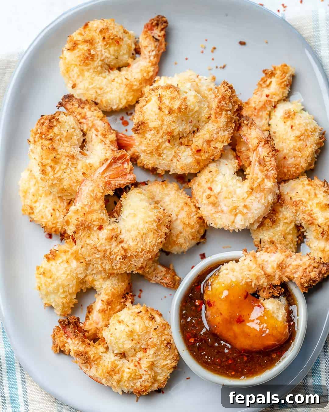 a single coconut shrimp in a dipping sauce bowl with more coconut shrimp next to the dipping sauce.