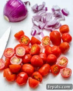 chopped tomatoes and sliced onions on a cutting board.