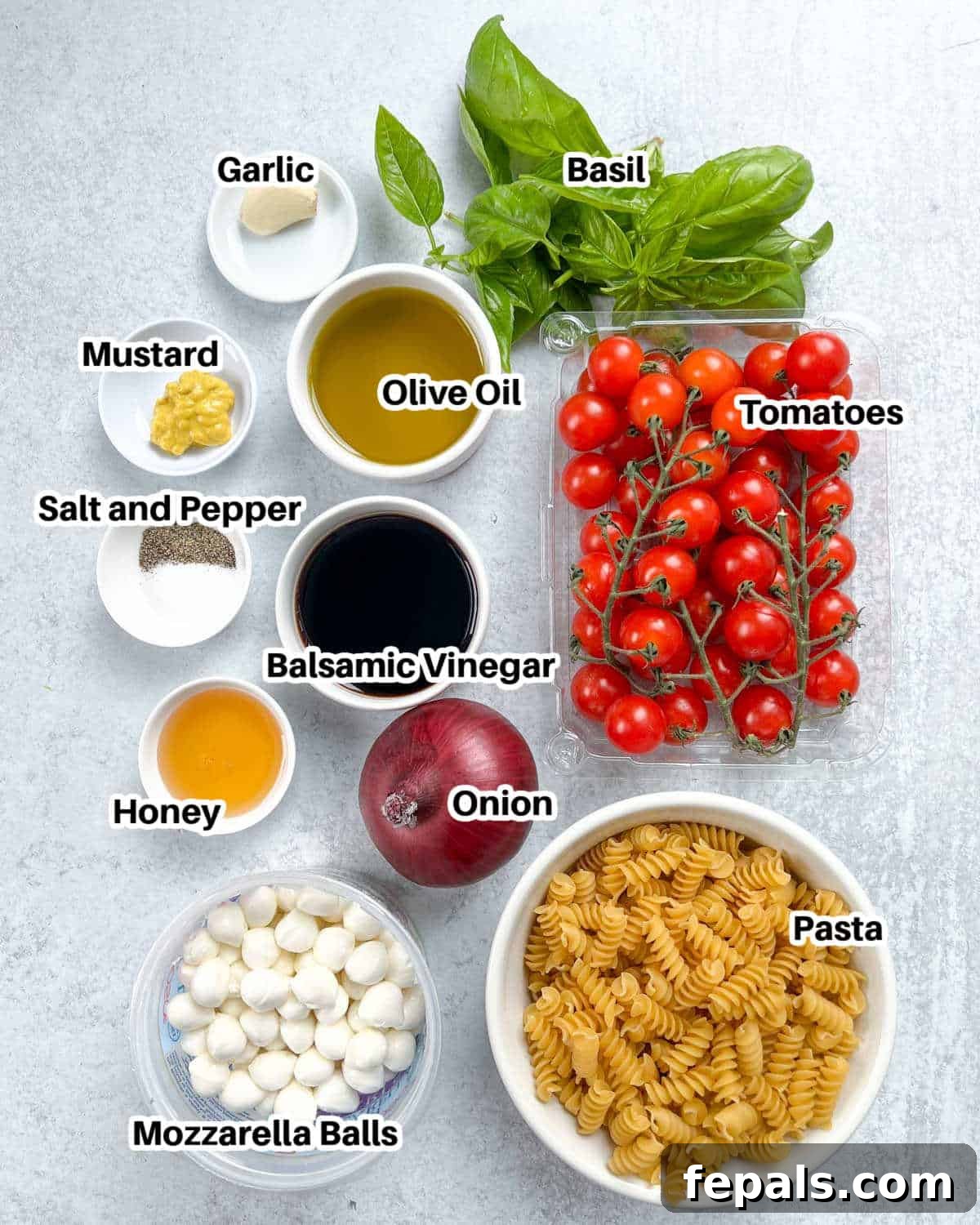Various fresh ingredients laid out on a wooden board to make Caprese pasta salad, including tomatoes, basil, mozzarella balls, pasta, and dressing ingredients.