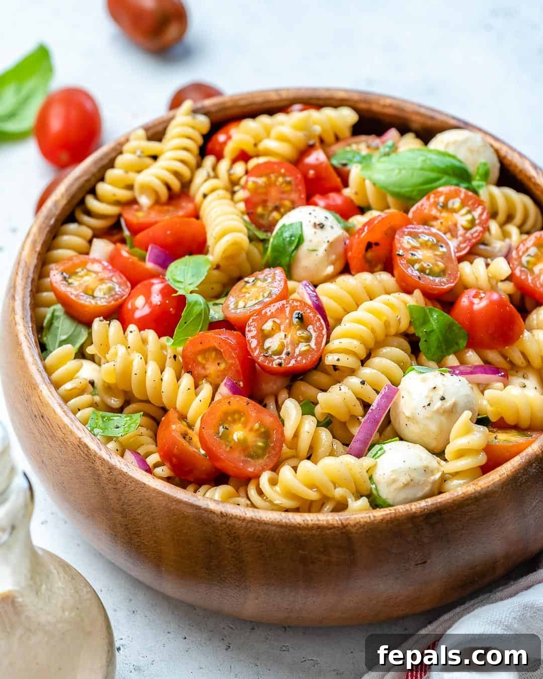 Close-up of Caprese pasta salad with cheese balls, fresh basil, and halved cherry tomatoes in a large bowl.