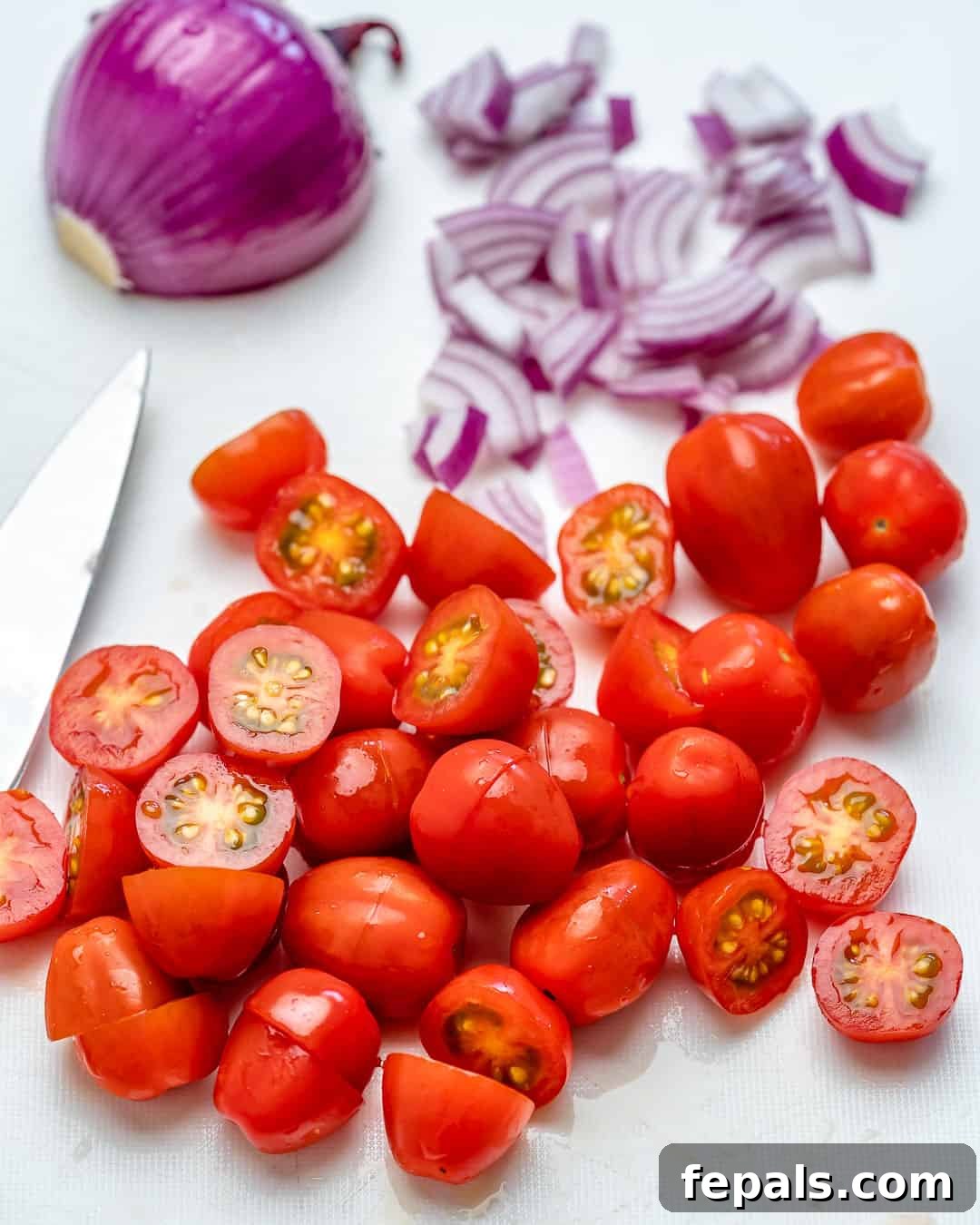 Chopped cherry tomatoes and thinly sliced red onions on a cutting board, ready for the salad.