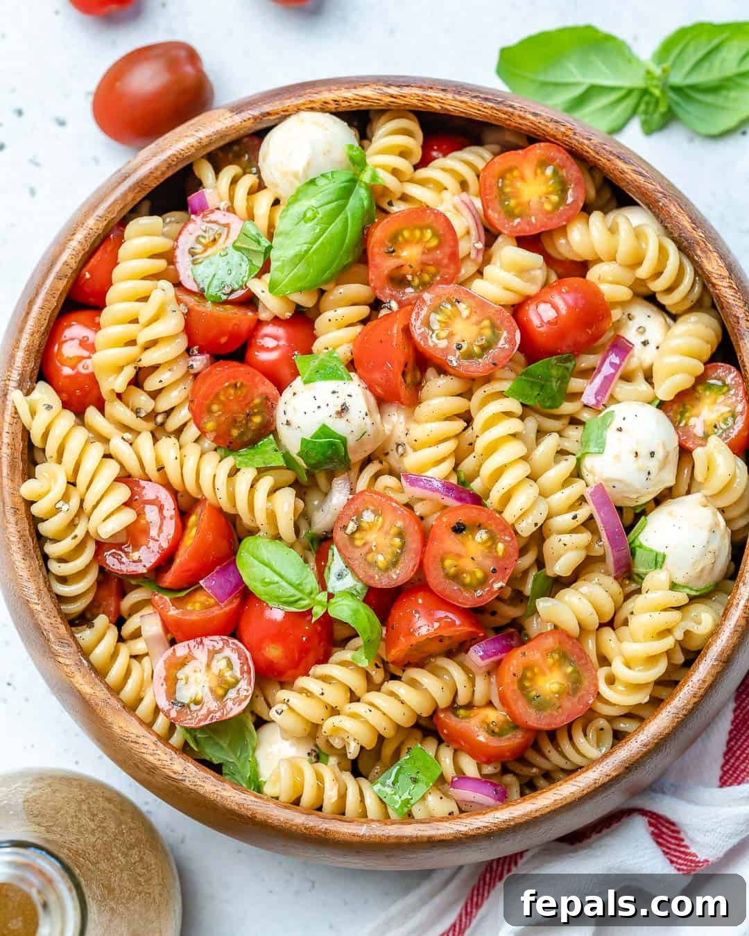 Caprese pasta salad served in a round wooden bowl, ready to be enjoyed.