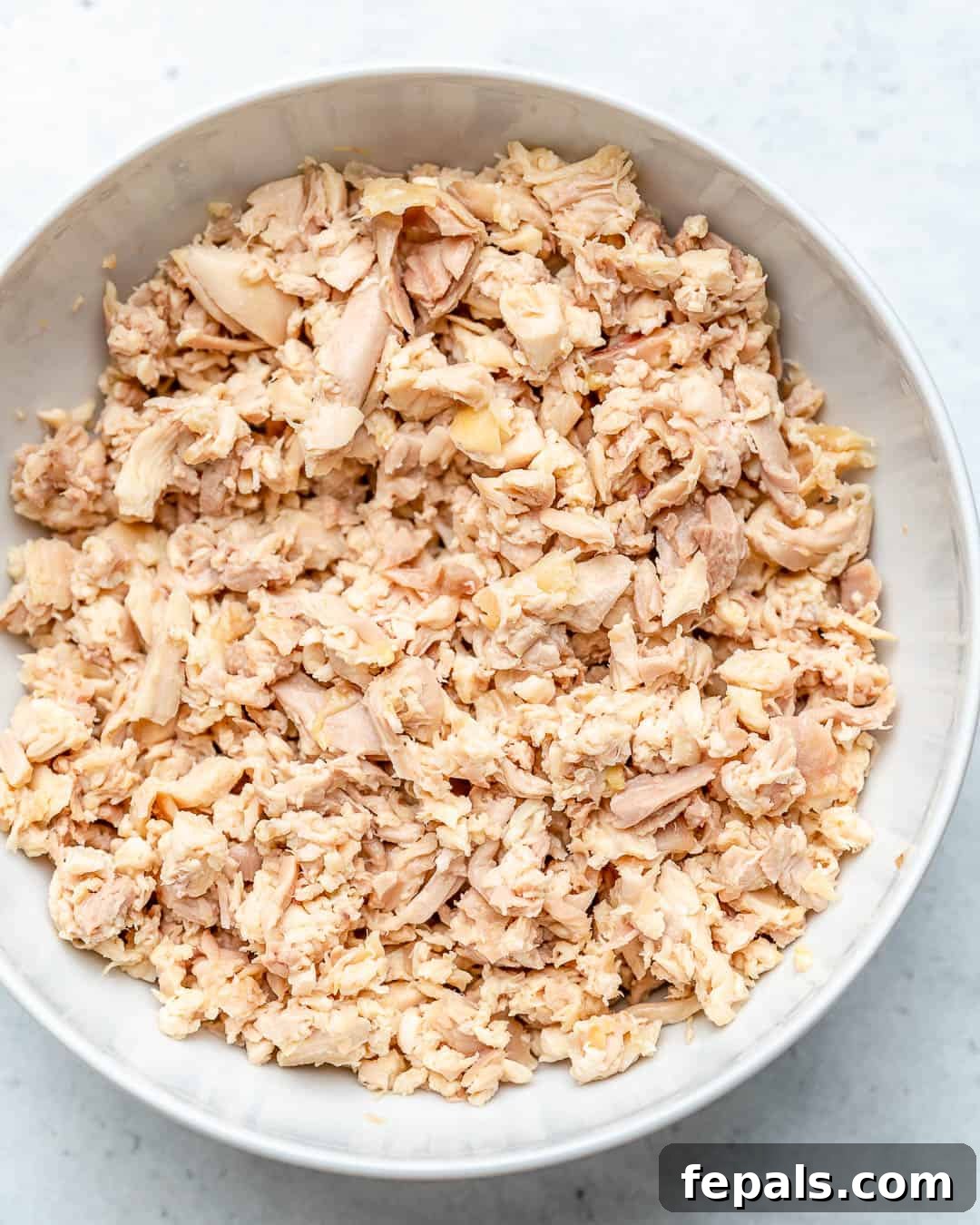 A bowl filled with finely shredded cooked chicken, ready to be mixed with sauce.