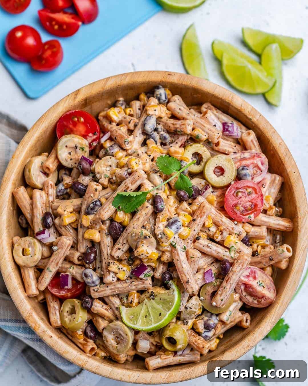 Sun-Kissed Southwest Pasta 2 Vibrant vegetarian Southwest pasta salad in a rustic round wooden bowl, garnished with fresh cilantro and a lime wedge.