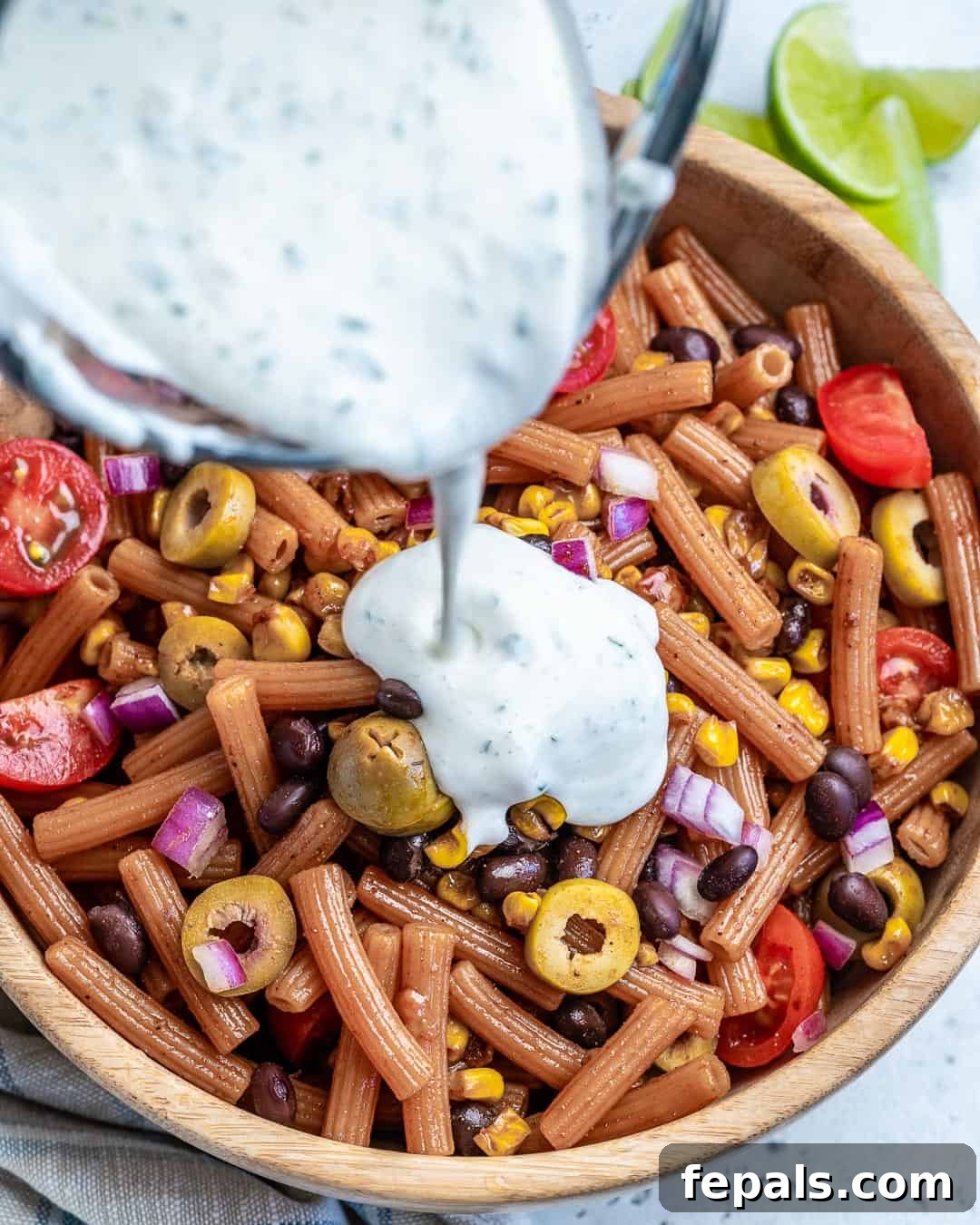 Sun-Kissed Southwest Pasta 4 Pouring the creamy Southwest dressing over a large bowl of pasta salad ingredients.