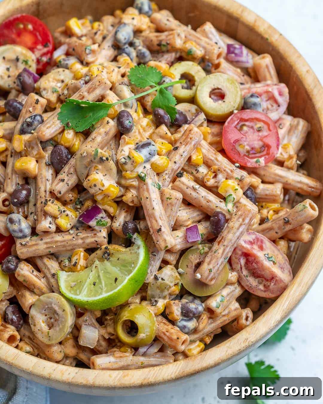 Sun-Kissed Southwest Pasta 5 A beautifully presented round wooden bowl of Southwest pasta salad, garnished with fresh herbs and a lime wedge, ready to serve.