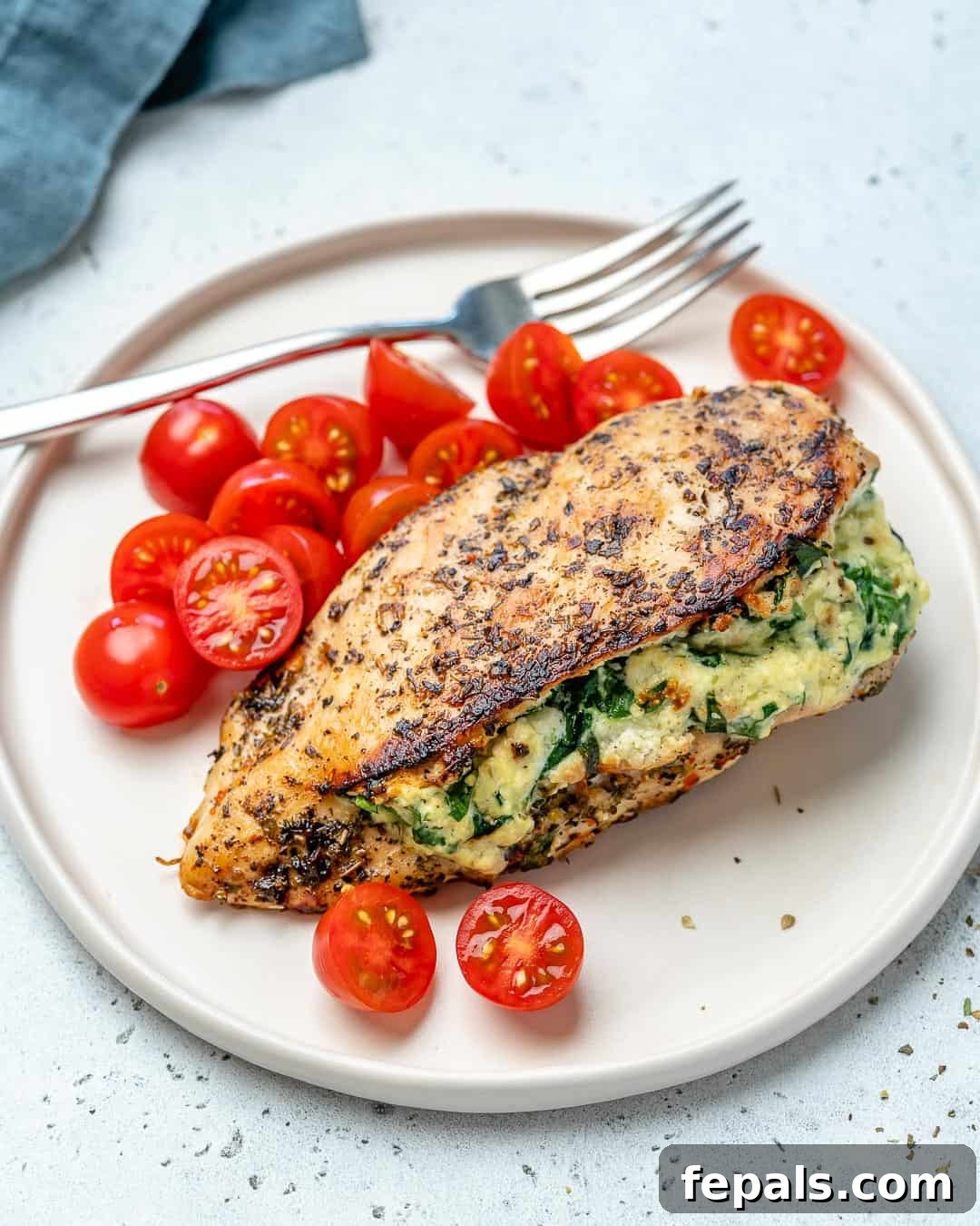 Creamy Spinach and Cheese Stuffed Chicken 9 Stuffed chicken breast on a plate with fresh tomatoes and herbs, ready to be served.