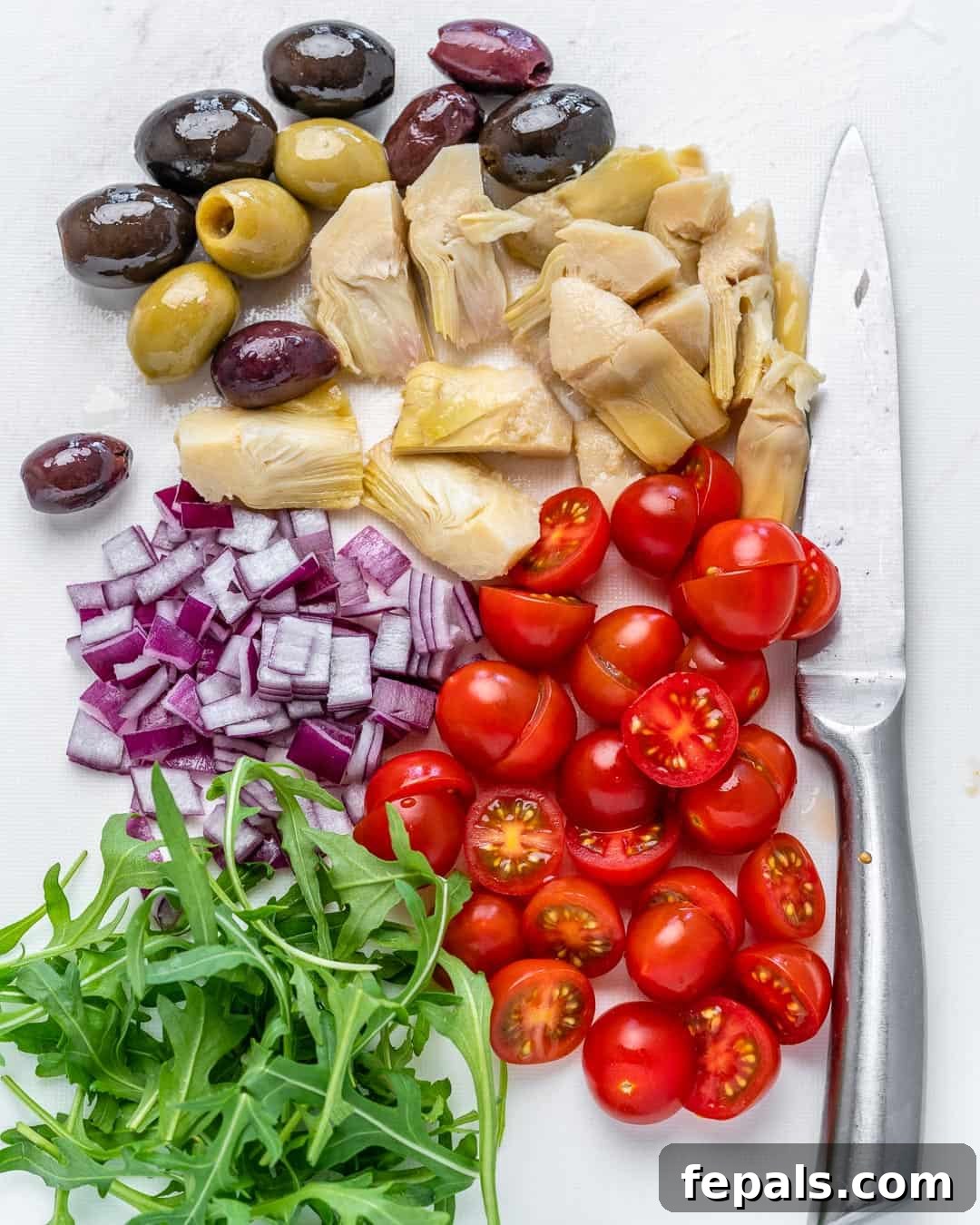 chopped pasta salad ingredients- tomatoes, onions, arugula, olives, and pickled artichoke