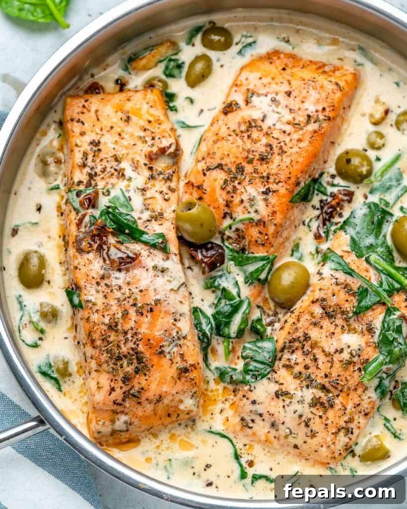 Overhead shot of perfectly cooked salmon fillets nestled in a creamy Tuscan sauce with spinach, sun-dried tomatoes, and olives in a skillet