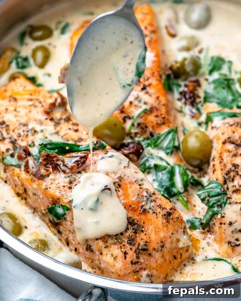 Close-up of creamy sauce being drizzled over a salmon fillet in a skillet, highlighting the rich texture and vibrant ingredients.