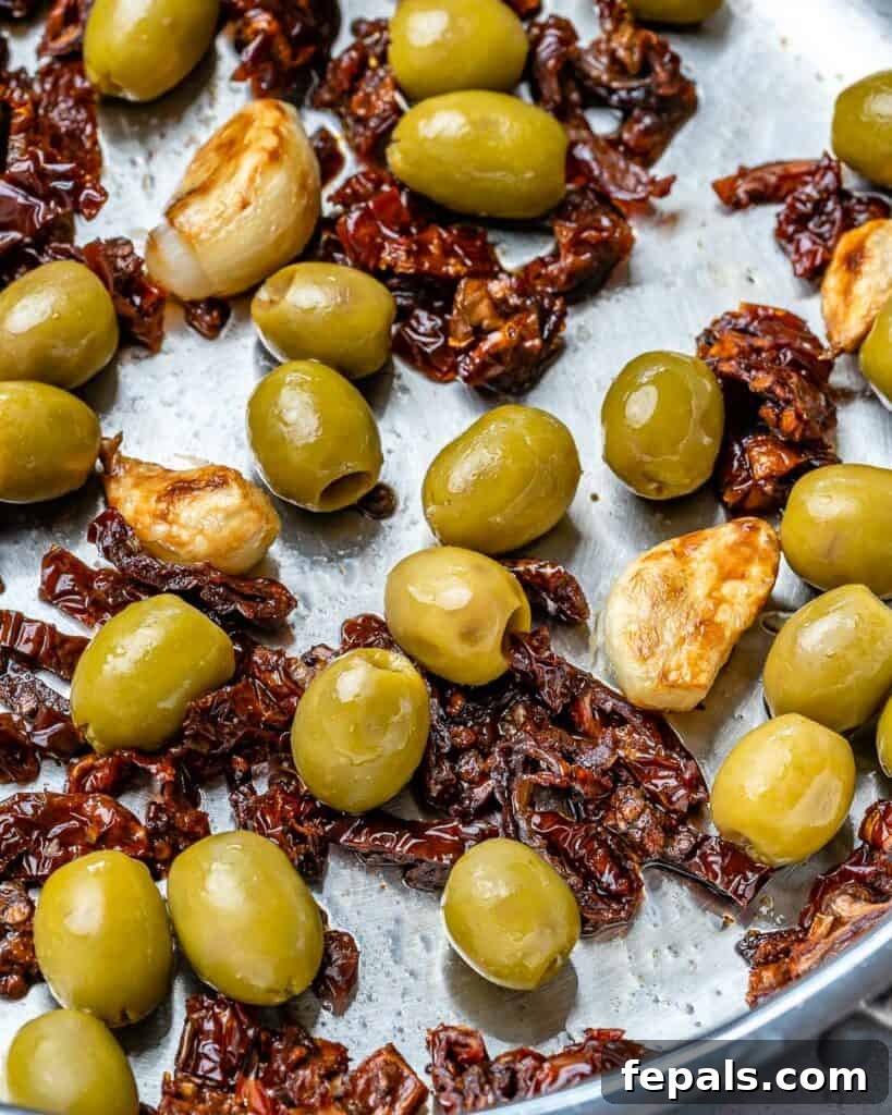 Olives and sun-dried tomatoes simmering in a pan with sautéed garlic, forming the flavorful base of the Tuscan sauce.