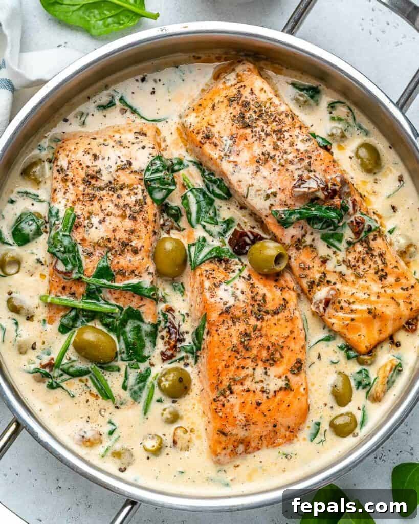 Top view of a skillet showcasing creamy pan-seared salmon nestled in the vibrant Tuscan sauce with visible spinach and olives.