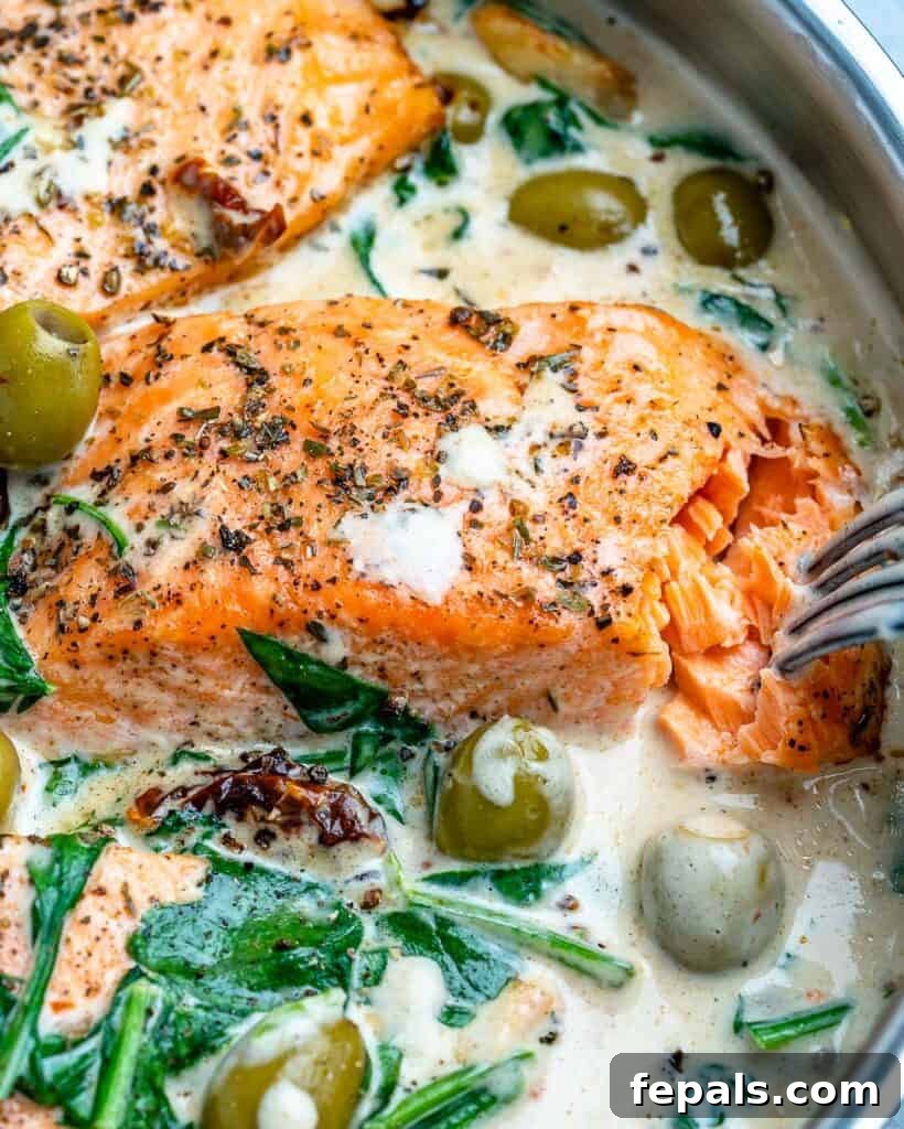 Close-up of a fork flaking cooked salmon in a pan with creamy Tuscan sauce, highlighting the tender texture.