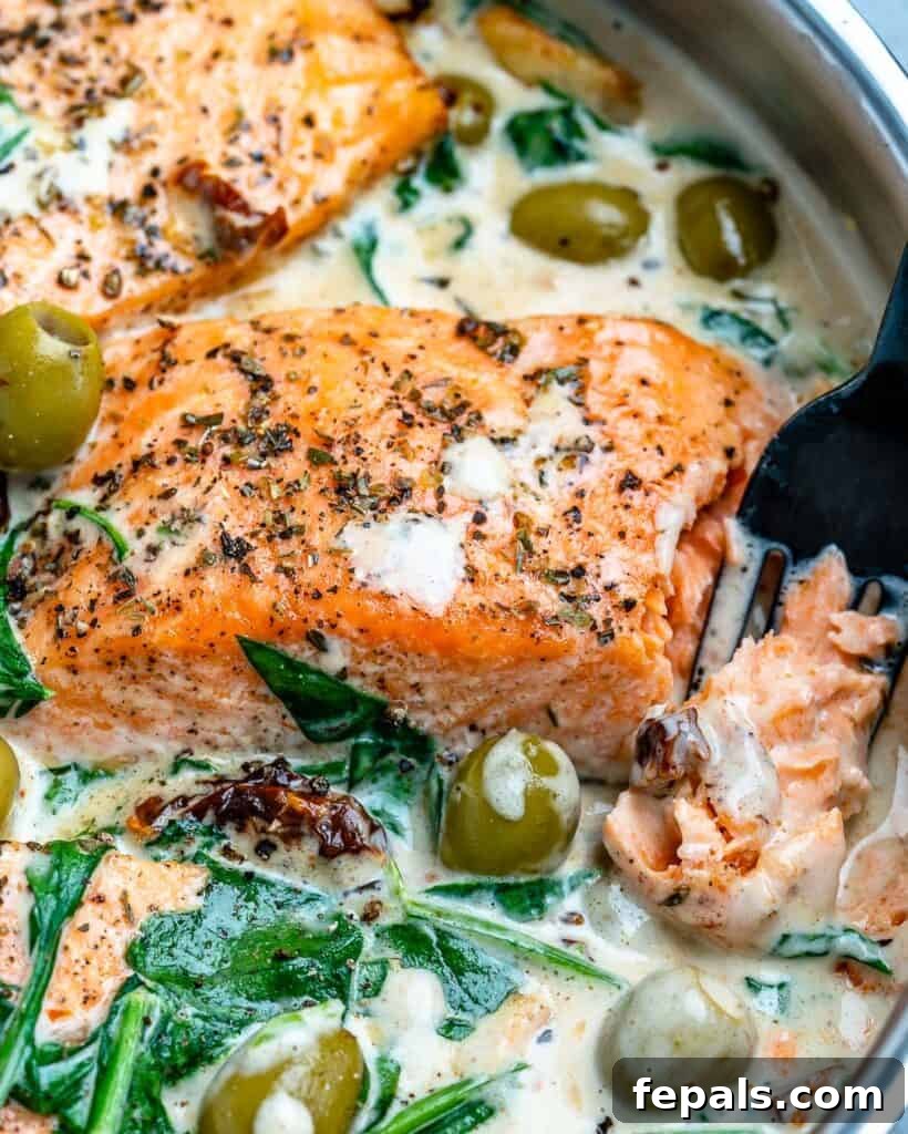 Fork in salmon flaking it in a creamy sauce in a pan, highlighting the perfect cook.
