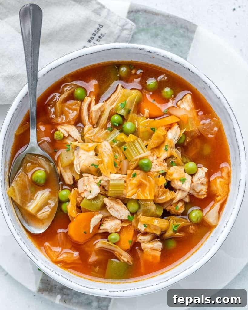 Top view of a white bowl of healthy chicken and veggie soup with a spoon.