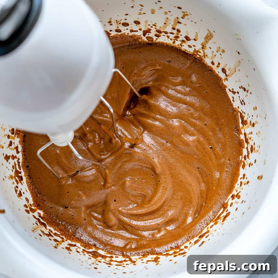 An electric mixer actively whipping the coffee mixture in a bowl, showing the beginning stages of the frothing process.